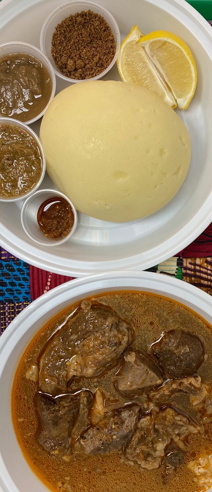 Two white bowls of West African food: fufu with sauces and lemon, and a meat stew.