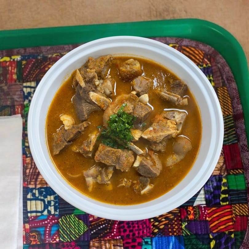Overhead view of a white bowl filled with a rich, orange-brown stew containing meat chunks and garnished with parsley.