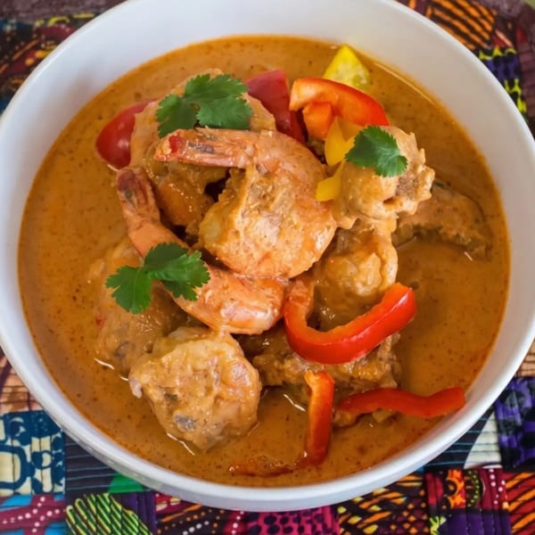 A white bowl filled with shrimp and chicken in a creamy orange sauce, garnished with bell peppers and cilantro.