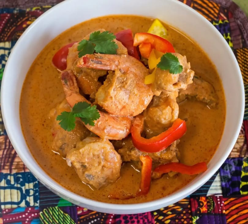 A white bowl filled with shrimp and chicken in a creamy orange sauce, garnished with bell peppers and cilantro.